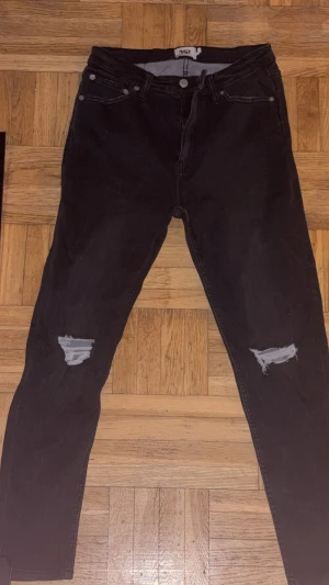 Svarta jeans med slitningar - Svarta jeans från 157, snygga slitningar vid knäna. Klassisk femficksmodell med knapp och dragkedja framtill. Perfekta för dig som gillar en edgy och trendig stil. helt oanvända