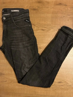 Replay Anbass svarta slim jeans - Svarta Replay Anbass jeans med slim fit och klassisk femficksdesign. Snygga detaljer med Replay-logga på fickan och metallknapp i midjan. Jeansen har en smal passform och är tillverkade i stretchigt denim för extra komfort.