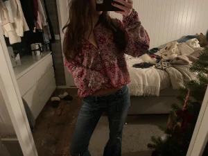 Rosa mönstrad croppad blus med dragkedja - Säljer en färgstark croppad blus i rosa och röda toner med ett unikt geometriskt mönster. Blusen har långärmade, lite puffiga ärmar och en dragkedja framtill som gör den extra cool. Perfekt för dig som gillar statement-plagg och vill sticka ut.