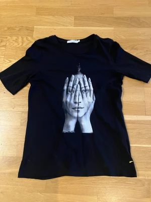 Svart t-shirt med grafiskt tryck - Säljer en svart t-shirt från Coster Copenhagen med ett unikt grafiskt tryck på framsidan. Klassisk rund hals och korta ärmar. Skön passform och mjukt material som känns nice mot huden. Perfekt för dig som gillar statement-plagg.