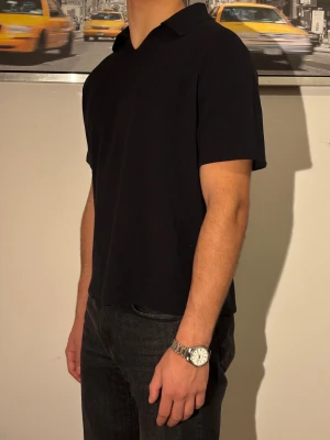 Svart Piké  - En stilren svart polotopp med korta ärmar och klassisk krage. Toppen har en rak passform och är tillverkad i mjukt bomullsmaterial som känns skönt mot huden. Perfekt för dig som gillar minimalistisk och clean stil.