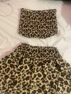 Leopardmönstrad bandeau tubtopp, matchande kjol - Säljer en bandeau tubtopp med leopardmönster i beige, brunt och svart. Toppen är smockad och har en stretchig passform som sitter snyggt på kroppen. Perfekt för dig som vill sticka ut och älskar djurmönster! Tillsammans med en matchande kjol