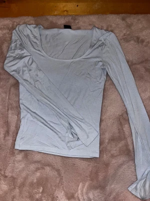 Ljusblå långärmad topp Gina Tricot - Supersnygg ljusblå långärmad topp från Gina Tricot i storlek XS. Modellen har en djup rundad halsringning och är figurnära med stretchigt material.