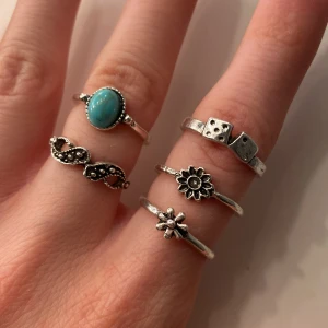 Fem silverfärgade ringar - Säljer ett set med fem tunna ringar i silverfärg. Några ringar har detaljer som blommor, tärningar och en oval turkos sten. Alla är helt oanvända och är ej äkta silver eller kristall. Alla för 10kr,  3kr styck! ❤️
