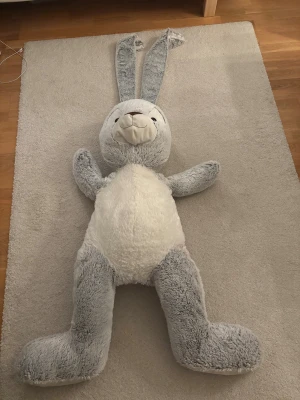 Mega gosedjurskanin 200cm hög - Pris går att diskutera! Detta är en stor, mjuk kanin-gosedjur i grått och vitt. Den har långa öron, ett vänligt ansikte och är perfekt som mysig inredningsdetalj eller leksak. Viss slitage syns på öronens kanter, en liten fläck där bak som syns på bilden men i övrigt är den i gott skick. Perfekt för barnrum eller som present. Frakt kommer till.