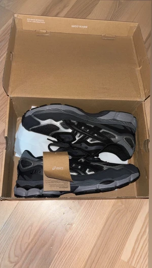 Svarta och grå Asics sneakers 43.5 - Säljer ett par snygga Asics sneakers i svart och grå med coola detaljer och mesh-paneler. Skorna har snörning och en platt sula som ger skön komfort. Perfekt för dig som gillar sportig stil och vill ha ett par stilrena sneakers med grym passform.