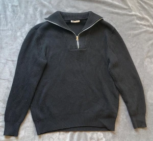 Svart ribbad stickad tröja från Zara - Svart stickad tröja från Zara med ribbad struktur och half zip-dragkedja framtill. Tröjan har en bred krage och långa ärmar, perfekt för dig som gillar en clean och stilren look. 