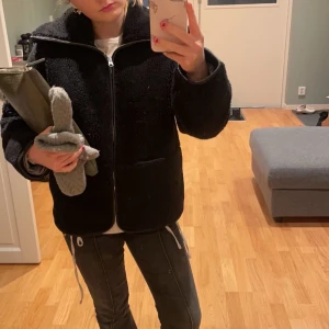 Svart teddyjacka med dragkedja - Säljer denna jättefina teddyjacka från arket. Den är ihopsydd i ena mudden på ärmen. Men annars fint skick. Jag är 165