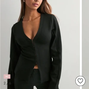 Svart kofta från Nelly med knappar - Svart tröja från Nelly i storlek M. Den har en enkel och clean design med v-ringad hals och knappar framtill. Långärmad och passar perfekt när du vill ha en stilren look. Materialet känns mjukt och skönt mot huden.