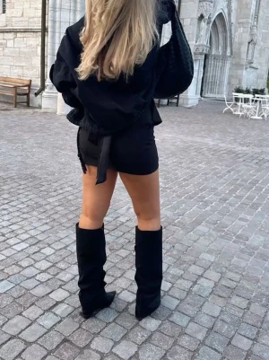 Svarta mockastövlar med klack - Säljer ett par svarta stövlar i mjuk mocka med hög klack och spetsig tå. Stövlarna har en slouchy passform och når upp till knäna, vilket ger en cool och trendig look. Perfekta att styla med kjol eller shorts för en edgy vibe. Helt nya med lådan kvar!❤️ Nypris 700-800kr