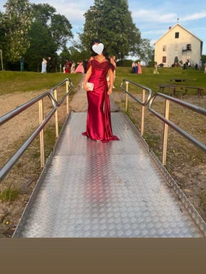 Röd balklänning/festklänning - Säljer en röd långklänning med glittrig paljettöverdel och offshoulder-ärmar. Klänningen har en snygg v-ringad urringning, markerad midja och ett elegant släp. Några få små hål lägst ner av klänningen men jag har kvar delen som jag sytt bort där nere som man får med. 