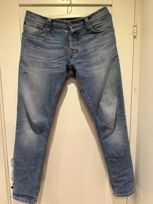 Ljusblå jeans från Nudie Jeans, W32 L32 - Säljer ett par ljusblå jeans från Nudie Jeans i storlek W32 L32. Det är modellen Grim Tim. Jeansen har klassisk femficksdesign, orangea sömmar och en rak passform. Tillverkade i mjukt denimtyg med snygga slitningar och subtila detaljer för en avslappnad look.