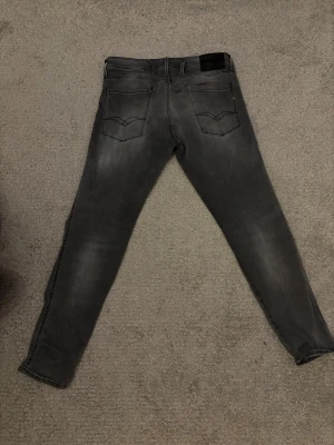Replay Anbass ljusgrå jeans - Snygga Replay Anbass jeans i ljusgrå tvätt med diskret slitning. Smal passform och klassisk Replay-logga på bakfickan. Jeansen är tillverkade i stretchigt bomullsmaterial för extra komfort och har raka ben med smal siluett. Köpts för ca 1300. Inga synliga defekter.
