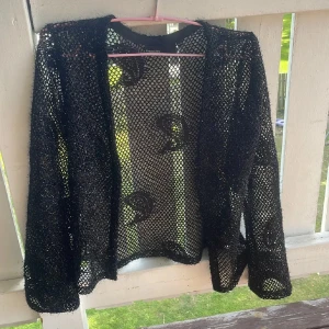 Svart glittrig cardigan jacka KappAhl - Svart glittrig cardigan jacka från KappAhl i storlek M. Jackan är stickad i ett nätmönster med lång ärm och har en öppen front utan knäppning. Perfekt för att ge din outfit lite extra edge med sitt glittriga material och transparenta look.