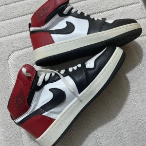 Nike Air Jordan 1 Chicago Highs - Säljer ett par Nike Air Jordan 1 Highs i den klassiska Chicago-färgställningen. Skorna har svart, vitt och rött skinn, ikonisk swoosh på sidorna och Air Jordan-logga på ankeln. Perfekta för dig som vill sticka ut med en tidlös sneakerlegend.