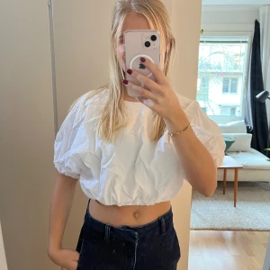 Vit croppad blus  - Säljer en vit croppad blus från Weekday med ballongärmar och rund hals. Toppen har en loose passform och är tillverkad i bomull. Elastisk kant nedtill ger en snygg siluett.