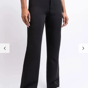 Svarta wide byxor med hög midja - Snygga svarta kostymbyxor med medel hög midja och raka, vida ben. Byxorna har en stilren look och är tillverkade i ett mjukt material som ger en skön passform. Perfekta för dig som gillar minimalistisk stil och vill ha ett plagg som är lätt att matcha.