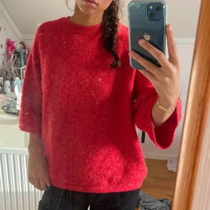 Röd stickad tröja med vida ärmar - Mysig röd stickad tröja med rund halsringning och trekvartsvida ärmar. Tröjan har en fluffig textur och en avslappnad passform som ger en chill vibe. Perfekt för att liva upp din höst- eller vintergarderob.