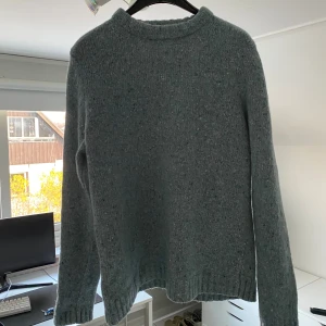 Arket stickad tröja  - Mysig gråblå stickad tröja med rund hals och ribbade muddar. Tröjan har en enkel och klassisk design med diskreta blå och ljusa inslag i garnet. Perfekt för kyliga dagar och passar till det mesta i garderoben.