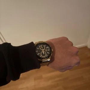 Guldfärgad klocka Santa Barbara Polo - Snygg guldfärgad klocka från Santa Barbara Polo & Racquet Club med svart urtavla och flera kronografer. Länken är i metall och har en klassisk, stilren design som passar perfekt till dig som gillar att sticka ut med accessoarer. Skick är som nyskick. Klockan köpte jag i ett köpcentrum i Budapest i Juni. Den är anpassad utefter min handled men resterande länkar följes med.