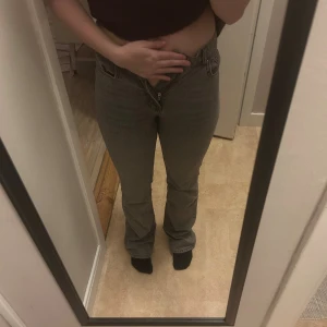 Grå bootcut jeans med medel midja - Säljer ett par gråa jeans med bootcut och medel midja. Jeansen har klassisk femficksdesign, dragkedja och knapp framtill. Materialet är jeans och passformen är normal med lite utsvängda ben. Perfekt för dig som gillar retrovibbar och snygg siluett.