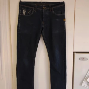 Mörkblå jeans från G-Star RAW W30 L34 - Snygga mörkblå jeans från G-Star RAW, modell 3301. Klassisk femficksdesign med G-Star patch bak och kontrastsömmar. Jeansen har en rak passform och är tillverkade i slitstarkt denimtyg. Perfekta för dig som gillar stilrena och tidlösa jeans.
