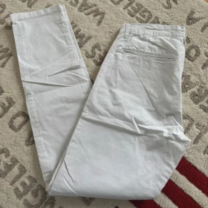 Vita chinos från Smog, storlek 30 - Snygga vita chinos från Smog i storlek 30. Byxorna har klassisk passform med raka ben, bälteshällor och fickor både fram och bak. Tillverkade i mjuk bomull som känns skön mot huden. Perfekt för dig som gillar stilrena och fräscha byxor.