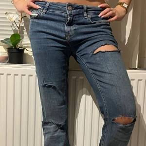 Blåa lågmidjade jeans med slitningar  - Säljer ett par blå low/midrise jeans med snygga slitningar och hål på knäna och låret (egengjorda). Modellen har klassisk femficksdesign, är bootcut och har normal midja. Passar runt 165 längd, storlek 34 HM. Aldrig använda endast testade! Hör av er vid frågor och funderingar 💞💝 