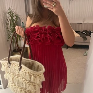 Röd omlottklänning med volang - Säljer en röd kortklänning med axelbandslös design och stora volanger upptill. Klänningen har plisserad kjol och omlottkänsla vid bysten, vilket ger en cool och romantisk vibe. Perfekt för dig som gillar att sticka ut med färg och detaljer.