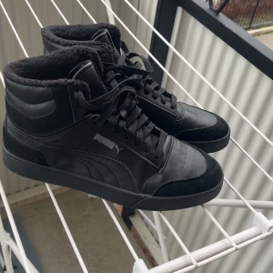 Svarta höga sneakers från Puma - Säljer ett par svarta höga sneakers från Puma med snörning och mjukt foder runt ankeln. Skorna är i skinn och mocka med klassisk Puma-logga på sidan. Perfekta för dig som gillar streetstyle och vill ha något som funkar året runt.