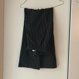 Svarta randiga kostymbyxor från Kappahl - Snygga svarta kostymbyxor från Kappahl med vita smala ränder. Klassisk rak passform och knappdetalj i midjan. Perfekta för dig som gillar stilrena och trendiga plagg. Materialet känns mjukt och bekvämt mot huden.