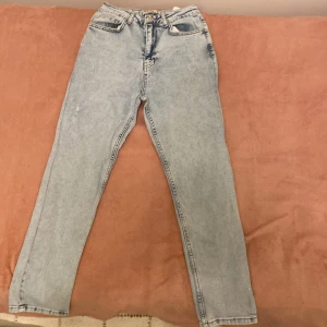 Ljusblå jeans från Vi Denim, strl 38 - Snygga ljusblå jeans från Vi Denim i klassisk femficksmodell. De har hög midja och raka ben med en straight fit. Jeansen är tillverkade i jeansmaterial och har knapp och dragkedja framtill. Perfekta för dig som gillar retrovibbar och enkel stil.