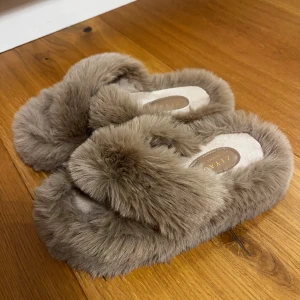 Beiga fluffiga sandaler från ZIYAO - Supermysiga sandaler från ZIYAO i beige färg med fluffig pälsimitation över hela skon. De har öppen tå och platt sula, perfekta att glida runt i hemma för en cozy vibe. Snyggt korsad design upptill och riktigt mjuka att ha på sig.