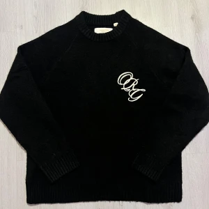 Svart stickad tröja  - Svart stickad tröja från Jack & Jones med broderad vit logga på bröstet. Tröjan har rund hals, ribbade muddar och lång ärm. Perfekt för dig som gillar enkel stil med en twist. Snygg att matcha med jeans eller chinos.