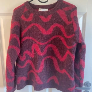 Stickad tröja från Carin Wester - Vinröd stickad tröja från Carin Wester i storlek S. Tröjan har ett vågigt mönster i rött och är gjord i ull. Den har rund halsringning och långa ärmar, perfekt för kyliga dagar💕