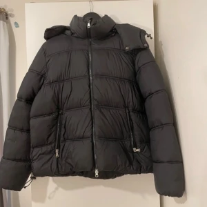 Svart pufferjacka från 157, storlek S/L - Märke: 157 Skick: Ny, aldrig använd (med taggar kvar)  Varm och snygg oversize dunjacka. Storlek S men passar även M–L beroende på önskad passform.  🧥 Detaljer: 	•	Avtagbar huva (med dragkedja) 	•	Två fickor med dragkedja 	•	Justerbar nedtill 	•	Tjock och mysig, perfekt för vintern  💸 Nypris ca 500 kr 📦 Skickas snabbt! 