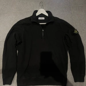 Svart half zip sweatshirt Stone Island - Svart sweatshirt från Stone Island med klassisk logotyp-patch på vänster ärm. Tröjan har half zip framtill, ståkrage och ribbade muddar. Tillverkad i mjuk bomull, perfekt för dig som gillar streetwear och vill ha en clean look. Nypris 3400kr 