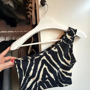 Svart/beige oneshoulder topp - 🤍Säljer en croppad topp med ”zebramönster” i svart och beige. Modellen är oneshoulder och har en tight passform som framhäver axlarna 🤍