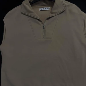 Beige väst med half zip från Stay - Stilren beige väst från Stay med hög krage och half zip-dragkedja framtill. Västen är ärmlös och har en clean look som passar perfekt för lager-på-lager outfits. Tillverkad i mjukt material för en bekväm känsla.