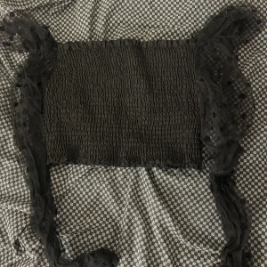 Svart smockad topp med meshärmar - Säljer en svart smockad topp med transparenta meshärmar som har prickigt mönster. Toppen är croppad och har en tight passform. Perfekt för dig som gillar trendiga detaljer och vill sticka ut med coola ärmar.