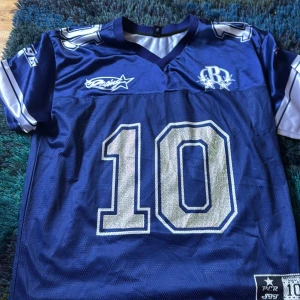 Blå fotbollströja från Romwe, stl L - Snygg blå fotbollströja från Romwe i storlek L. Tröjan har korta ärmar, V-ringning och stora vita siffror (10) framtill. Materialet är lätt och andas, perfekt för match eller träning. Silverfärgade detaljer och tryck på axlarna ger en sportig look. Har använt en gång till Billie konserten. Har normalt xs-s i kläder och den passar mig men den är oversized ( som jag ville ha ) 