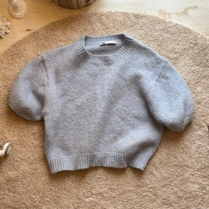 Ljusgrå stickad tröja från Zara - Superfin ljusgrå stickad tröja från Zara med korta puffärmar och ribbad halsringning samt nederkant. Tröjan har en mjuk och mysig känsla, perfekt för lager-på-lager och chill stil. Enkel design som ändå känns trendig och fräsch.