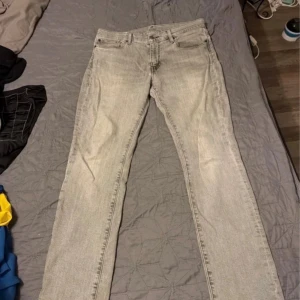 Levis 511 ljusgrå jeans straight fit - Säljer ett par Levis 511 jeans i ljusgrå tvätt med klassisk straight fit. Byxorna har fem fickor, knappgylf och Levis patch bak i brunt läder. Materialet är mjukt jeans och passformen är normal. Perfekt för dig som gillar en clean och enkel look.