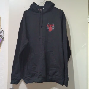 Svart Smash Into Pieces hoodie XL - Svart hoodie från JustHoods i storlek XL med Smash Into Pieces-tryck på ryggen och coolt rött logomärke med eldflammor på bröstet. Klassisk känguruficka, snörning i huvan och mjukt material. Perfekt för dig som gillar bandmerch och streetstyle.