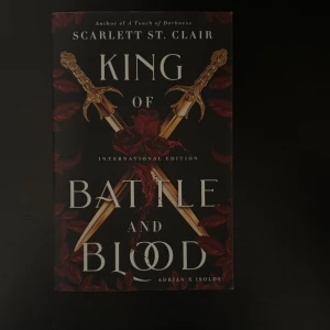 King of Battle and Blood - En internationell utgåva av 'King of Battle and Blood' av Scarlett St. Clair. Omslaget pryds av två korsade svärd och röda rosor, vilket ger en episk och mystisk känsla. Perfekt för dig som gillar spänning, fantasy och starka karaktärer.