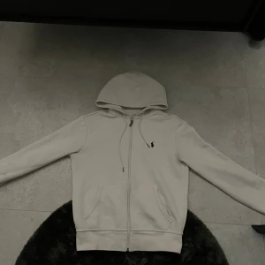 Polo Ralph Lauren Zip-Hoodie - Snygg vit hoodie från Polo Ralph Lauren i storlek XS. Tröjan har huva med snörning, dragkedja framtill och två fickor. Klassisk svart Polo-logga broderad på bröstet. Mjuk bomullskvalitet som är skön att ha på sig och passar perfekt till chill dagar. ‼️KVITTO FINNS‼️
