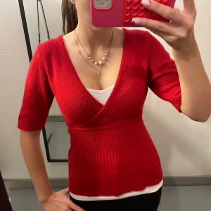 Röd omlottopp med ribbad midja - Snygg röd omlottopp med v-ringning och ribbad midja. Toppen har korta ärmar och är croppad i modellen. Perfekt för dig som gillar en feminin och trendig stil. Passar dig som vill sticka ut med färg och form.