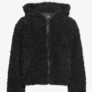 Svart teddyjacka med dragkedja - Mysig svart teddyjacka med fluffig yta och dragkedja framtill. Jackan har långärmade ärmar och en enkel, stilren design som passar perfekt när du vill ha en chill och varm look. Materialet är syntetiskt och ger en skön känsla.
