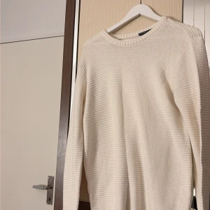 Vit stickad tröja från Livergy - Säljer en vit stickad tröja från Livergy i storlek L. Tröjan har en rund halsringning, ribbade muddar och ett snyggt, diskret ribbat mönster över hela plagget. Perfekt för dig som gillar enkel och clean stil.