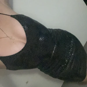 Svart glittrig kort klänning - Supersnygg svart glittrig klänning med smala axelband och figurnära passform. Klänningen har en v-ringad urringning och är täckt av glittrande paljetter som fångar ljuset. Perfekt för dig som vill sticka ut och glänsa.